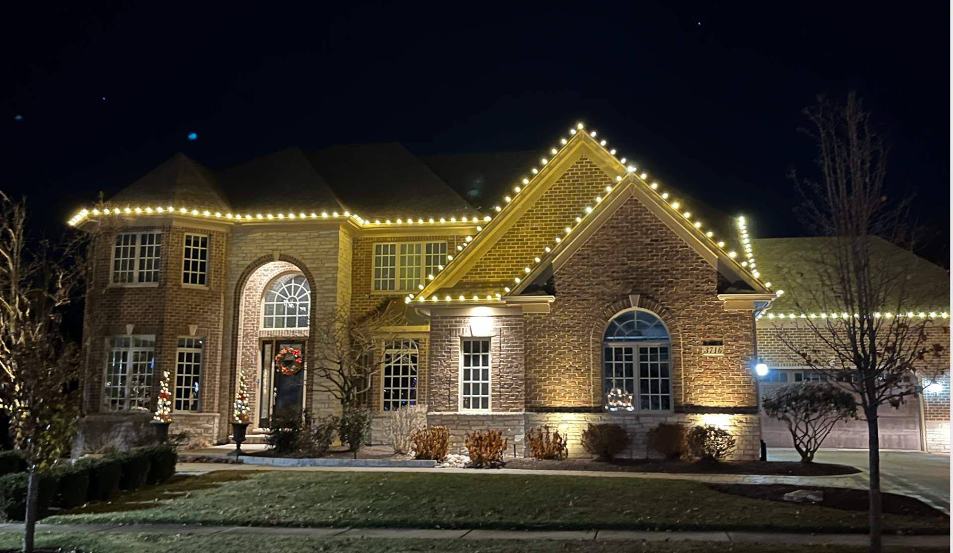 Stately brick home with warm white C9 roofline lights at night