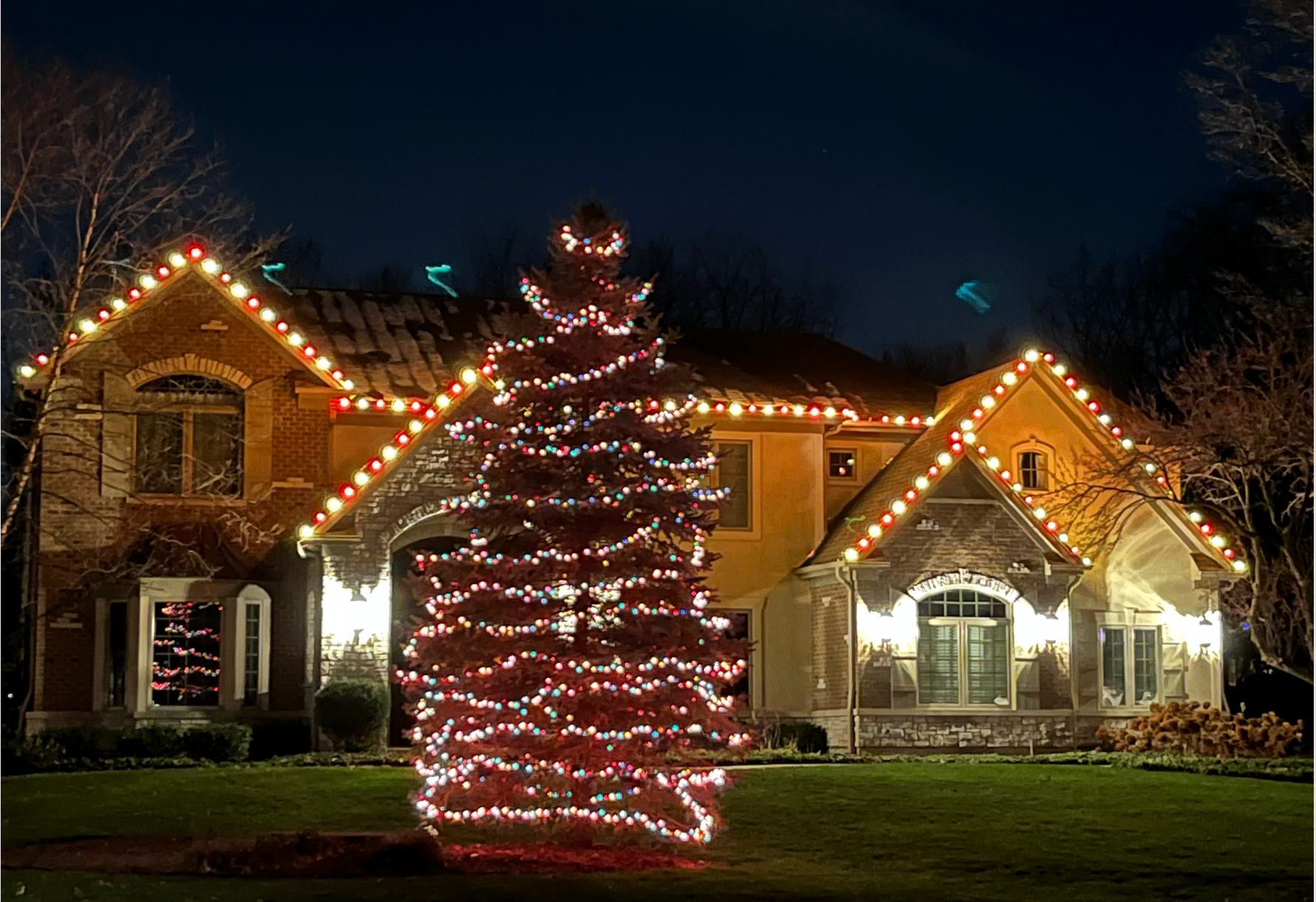 Brick home with red and white C9 roofline lights and lit pine tree