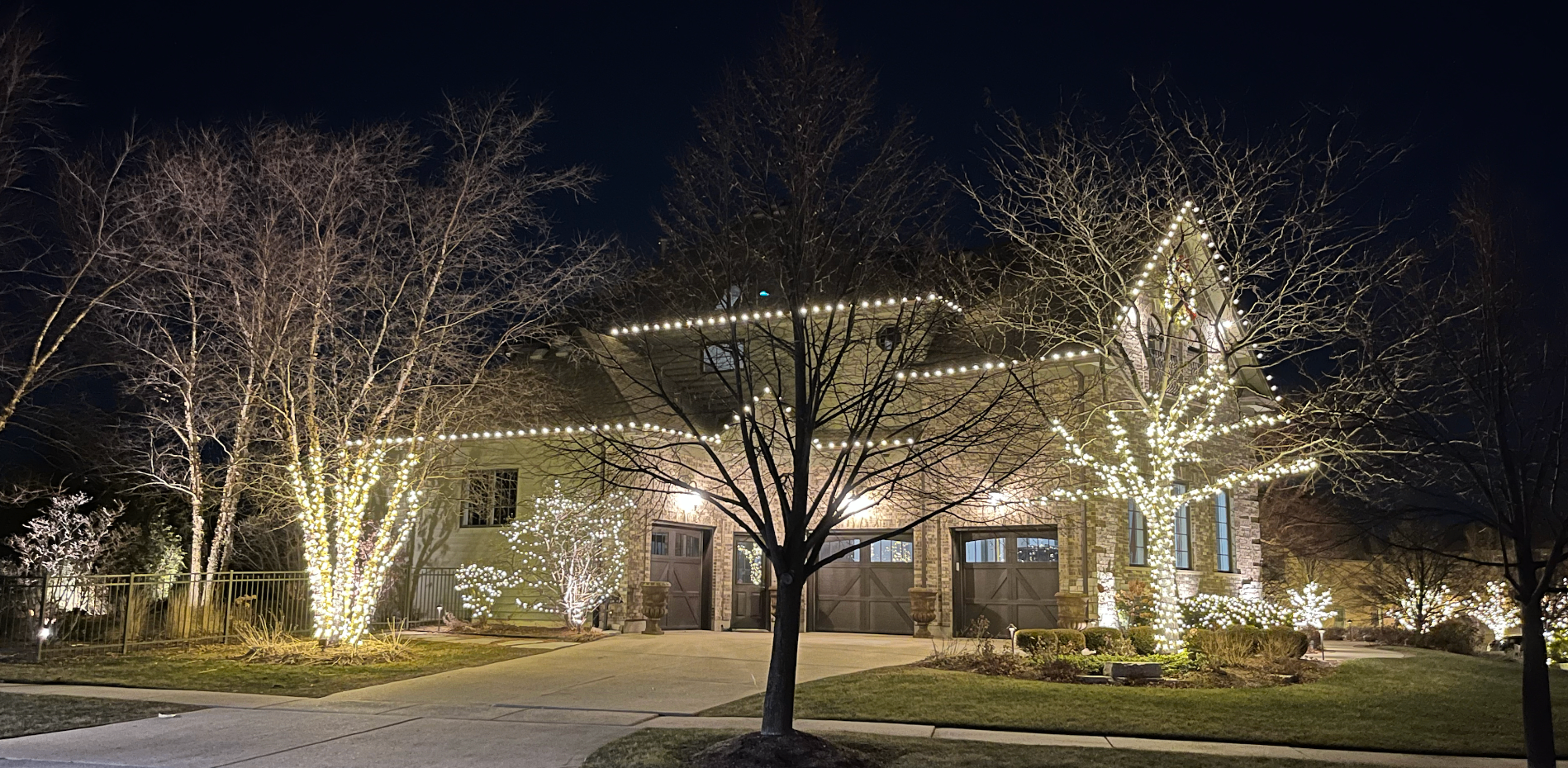Home with wrapped trees and crisp warm white roofline lights