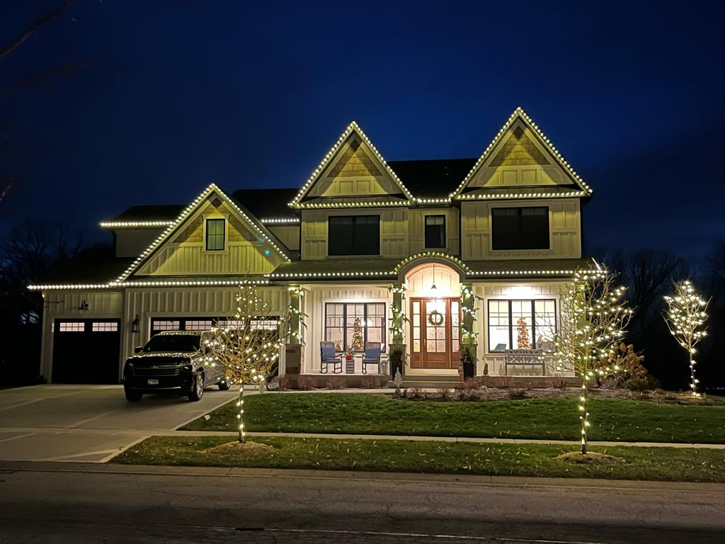 Elegant home with warm white roofline and wrapped tree lighting
