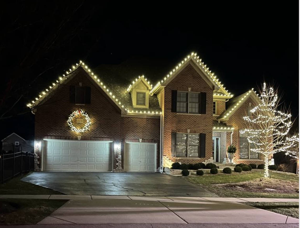Brick home with warm white roofline lights and lit tree