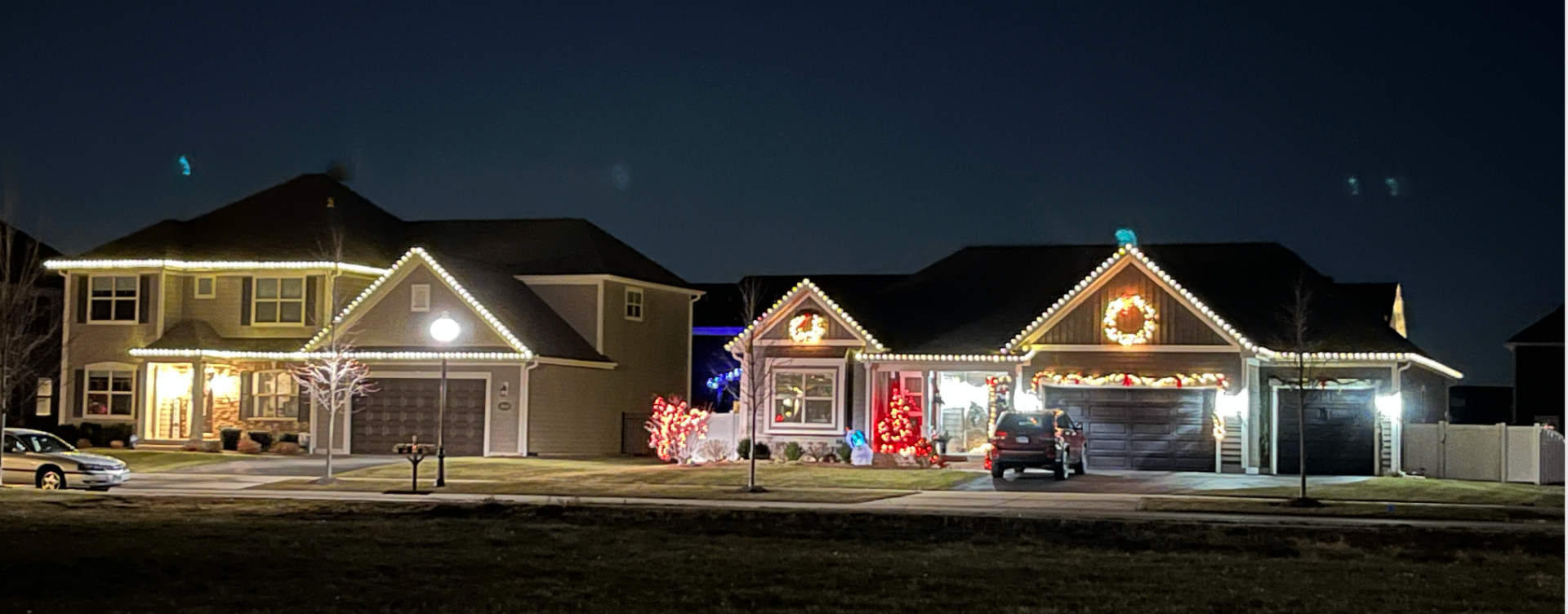 Neighborhood homes with warm white roofline lights and wreaths